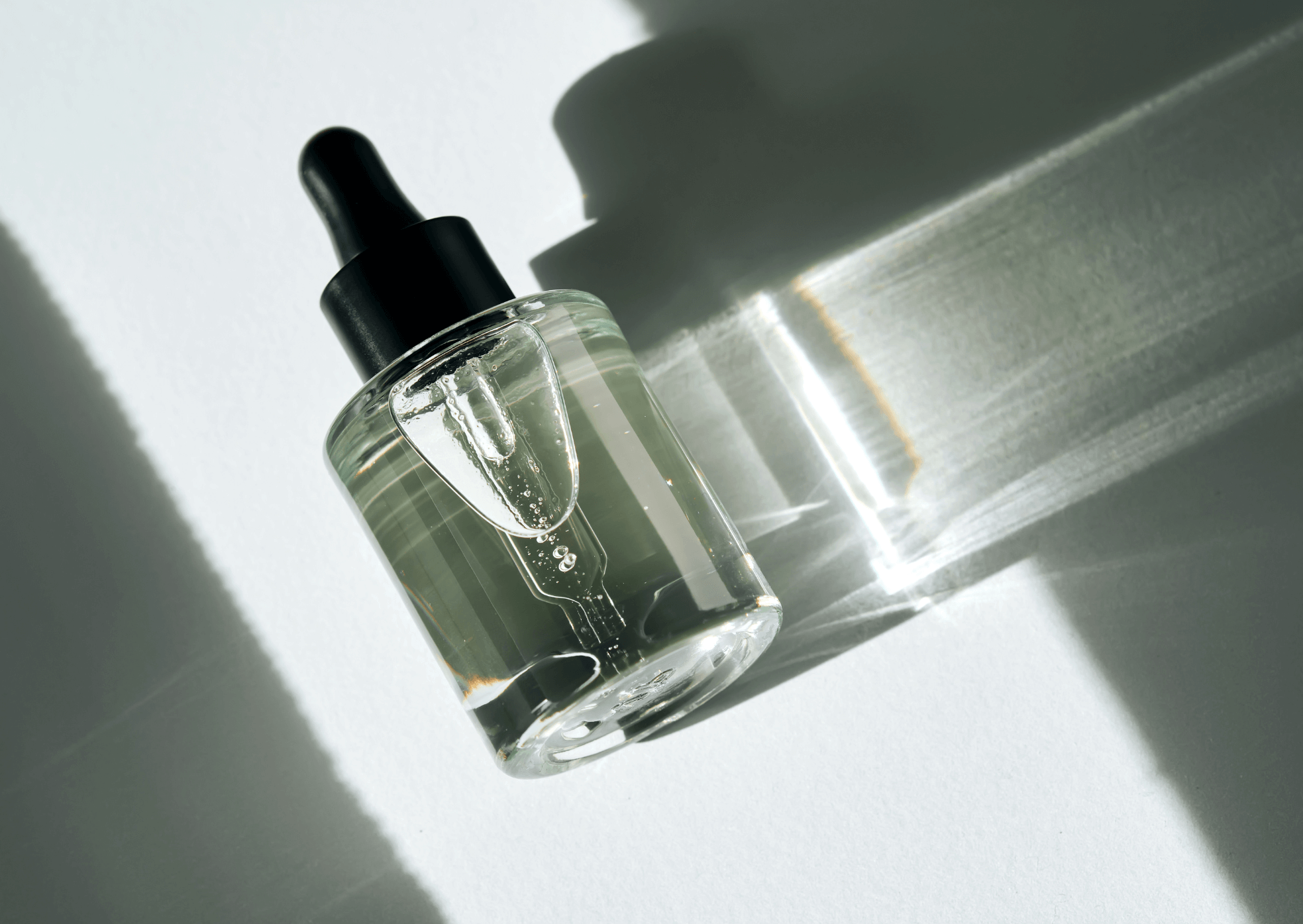 Clear glass dropper bottle with black cap on a light gray background