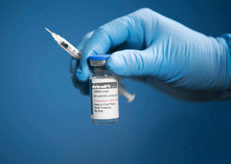 Hand in blue glove holding a syringe and vial against a blue background